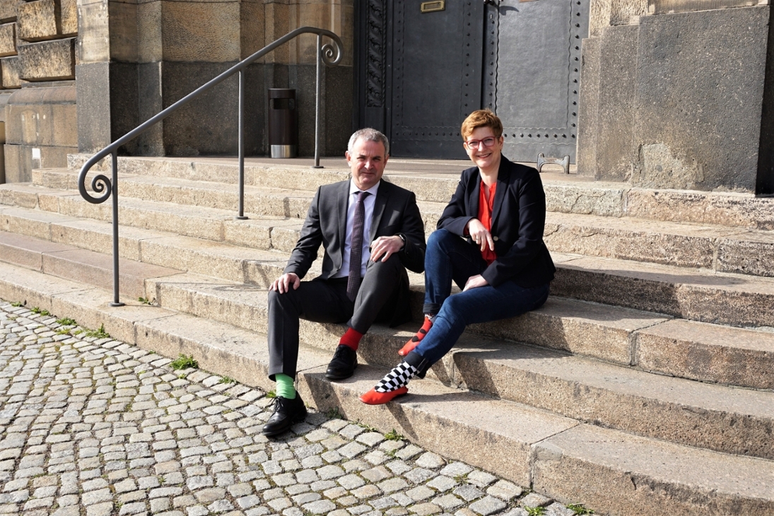 Die beiden Beauftragten, Herr Welsch und Frau Rüthrich, sitzen zum Welt-Down-Syndrom-Tag mit bunten Socken auf der Treppe vor der Sächsischen Staatskanzlei .