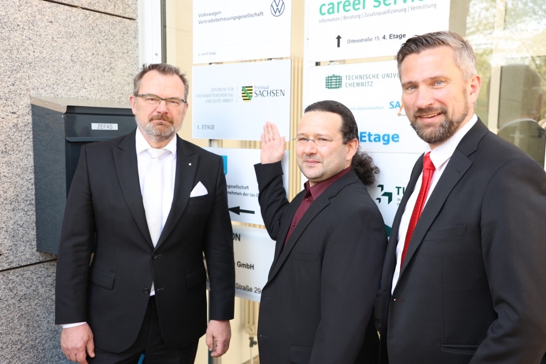 v.l.n.r.: Klaus-Peter Hansen, Vorsitzender der Geschäftsführung der Regionaldirektion Sachsen der Bundesagentur für Arbeit, der Leiter des ZEFAS, Dr. Matthias Geißler und Wirtschafts- und Arbeitsminister Martin Dulig stehen vor dem Eingang des Zentrum für Fachkräftesicherung und Gute Arbeit. Herr Geißler zeigt auf das Schild des Fachkräftezentrums.