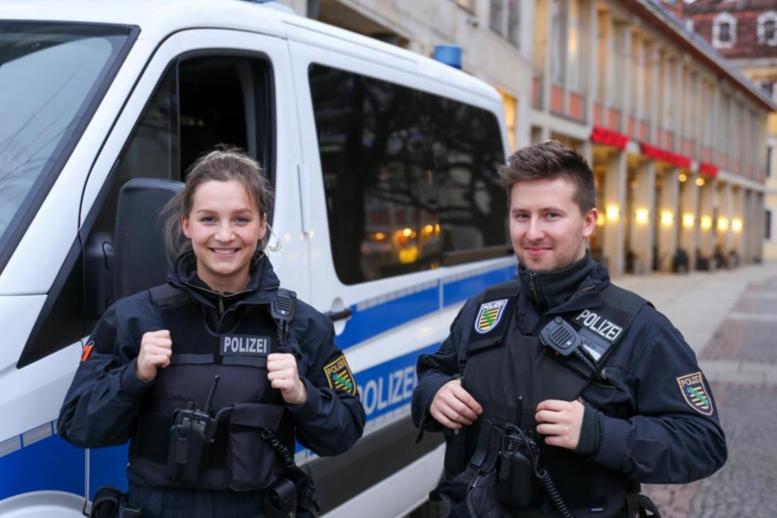 Eine Beamtin und ein Beamter der sächsischen Bereitschaftspolizei vor einem Einsatzfahrzeug.