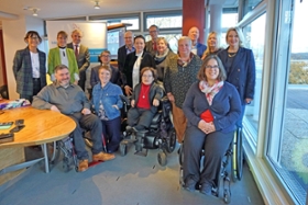 Foto: Die Beauftragten von Bund und Ländern für Menschen mit Behinderungen stehen in einem Raum in einer Gruppe zusammen und schauen in die Kamera.
