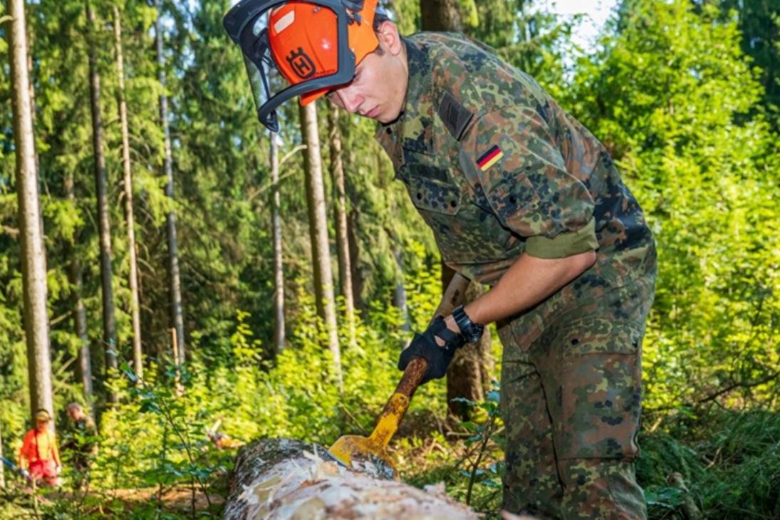 Ein Bundeswehrsoldat schält die Rinde von einer befallenen Fichte.