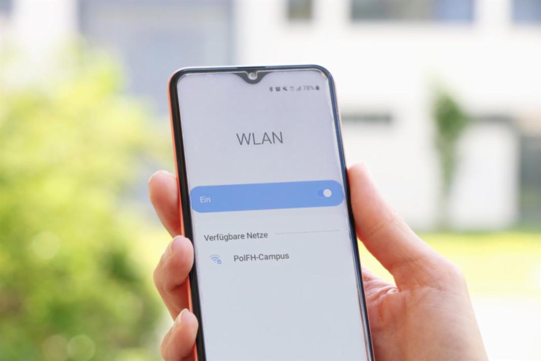 Smartphone in der Hand einer Person auf dem Campus der PolFH