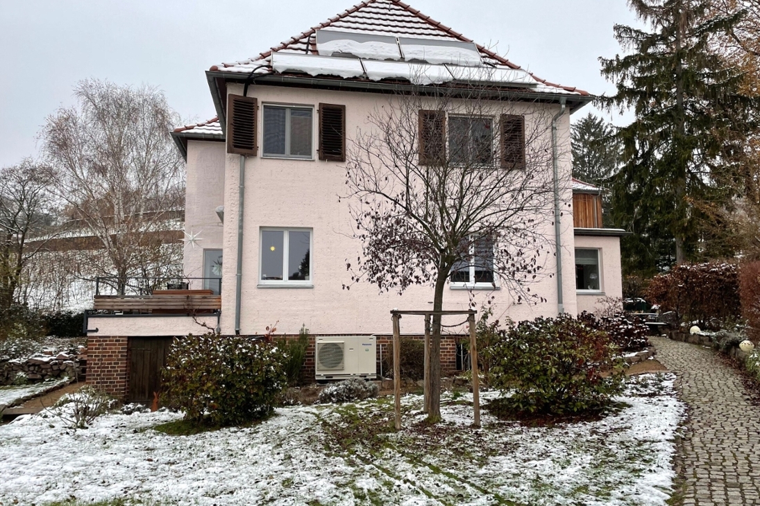 Luft-Wärmepumpe vor einem alten Wohngebäude im Winter.