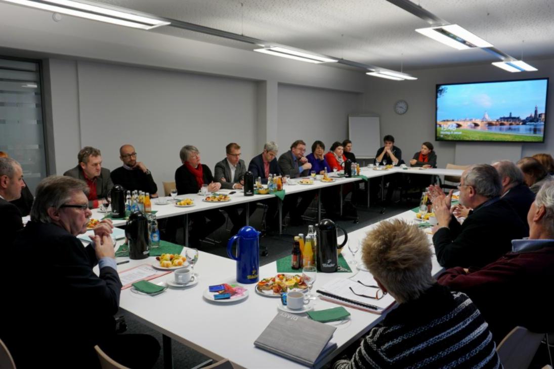 Verschiedene Teilnehmer des Neujahrsdialoges des Beauftragten der Sächsischen Staatsregierung für die Belange von Menschen mit Behinderung sitzen an einer U-Tisch-Formation und sind im Gespräch miteinander.