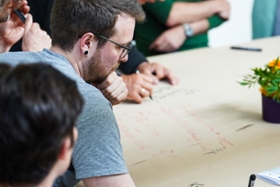 Foto: Teilnehmer eines Workshops notieren ihre Ideen und Gedanken auf ein großes Pergament auf einem der Diskussionstische.