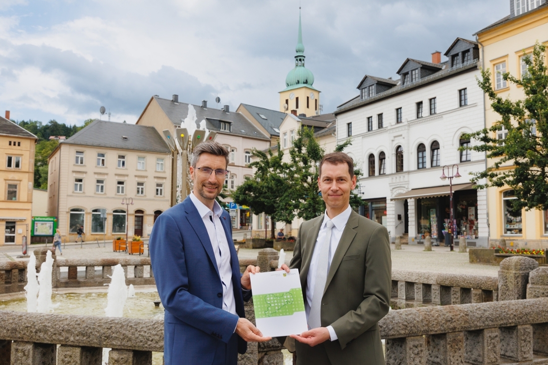 Der Präsident der Landesdirektion Sachsen, Béla Bélafi (rechts im Bild), übergibt dem Oberbürgermeister der Großen Kreisstadt Sebnitz, Ronald Kretzschmar, eine Bedarfszuweisung in Höhe von 1,4 Millionen Euro für die Ausrichtung des Tag der Sachsen 2025.
