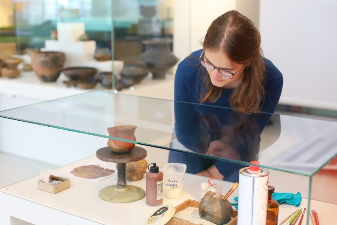Kuratorin Linda Seifert betrachtet eine Vitrine mit Arbeitsmaterialien der Restaurierung wie Gipskleber und Pinsel.