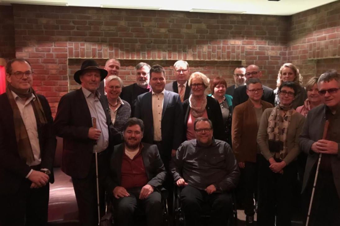 Für das Gruppenbild zum 57. Treffen in Düsseldorf stehen die Behindertenbeauftragten des Bundes und der Länder in einer Gruppe vor einer Ziegelwand.