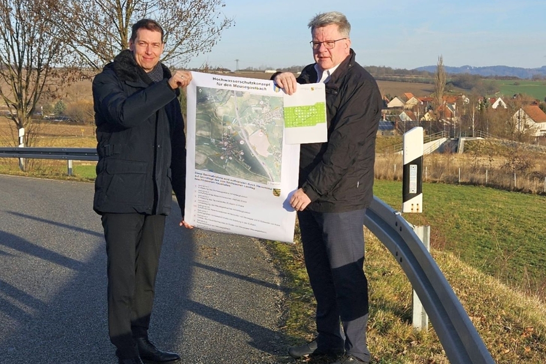 LDS-Präsident Béla Bélafi und der Dohnaer Bürgermeister Dr. Ralf Müller bei der Übergabe des Zuwendungsbescheides (v. l.). Im Hintergrund das fertiggestellte Hochwasserrückhaltebecken oberhalb des Ortsteils Krebs.