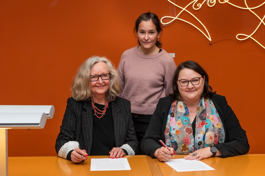 Maraike Wittbrodt (links, Tochter von Ursula Winnington) und Katrin Stump (rechts, Generaldirektorin der SLUB) unterzeichnen den Schenkungsvertrag zur Übernahme des Nachlasses von Ursula Winnington. In der Mitte: Enkelin Lilly Böhm