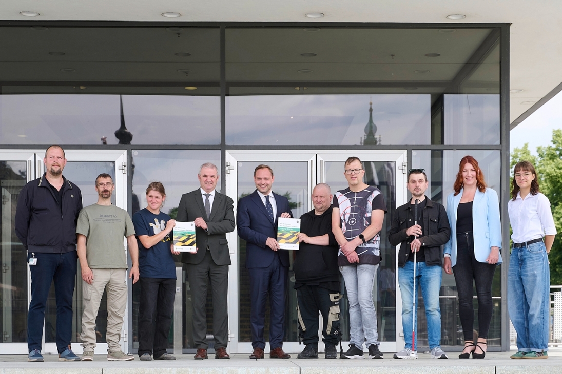 Landtagspräsident Alexander Dierks und Landesbeauftragter Michael Welsch mit Werkstatträten verschiedener WfbM und Mitarbeitenden des Projekts "Mittendrin in Markkleeberg" auf der Freitreppe vor dem Plenargebäude des Sächsischen Landtags bei der Übergabe der sächsischen Verfassung in Leichter Sprache