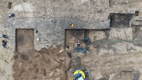 Foto: Mitarbeiterinnen legen das Hockergrab frei. Im oberen Bildrand erkennt man die Verfärbungen der Pfostengruben im Planum.